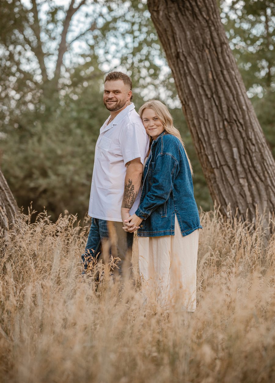Abby and Jacob standing in tall golden grass under a cottonwood tree